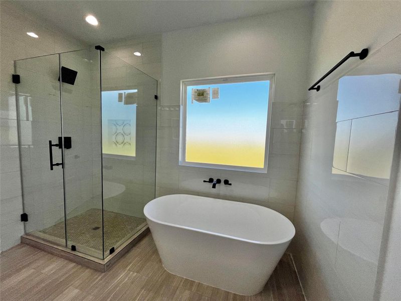 This bathroom features a modern design with a sleek freestanding tub, a spacious glass-enclosed shower, and stylish black fixtures. Natural light fills the space through a large window, complementing the neutral tile flooring and walls.