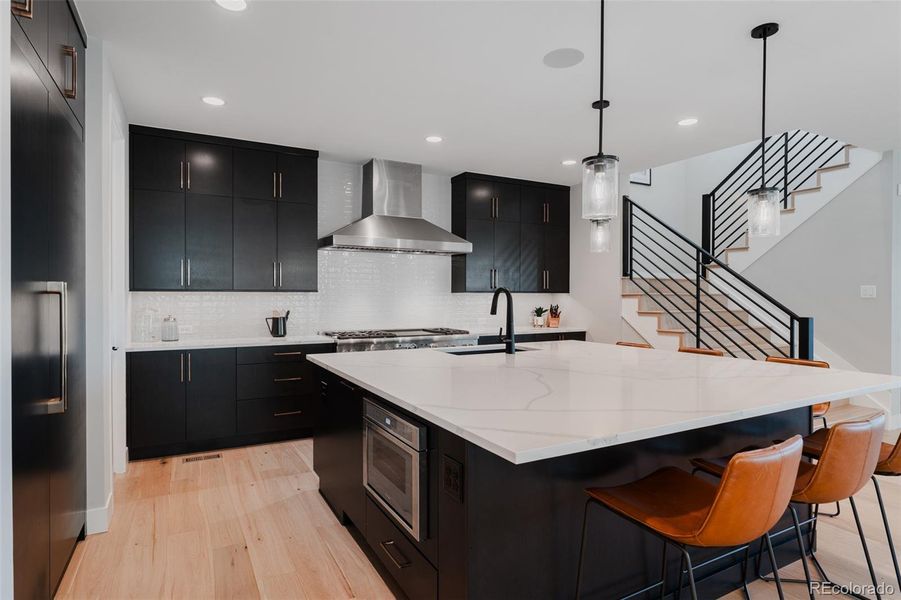 Ebony flat-paneled cabinets, adorned with exquisite champagne hardware, exude modern sophistication, beautifully contrasted by white subway tile and delicately veined white quartz countertops. An impressive Thermador built in refrigerator is carefully integrated with a cabinet facade.