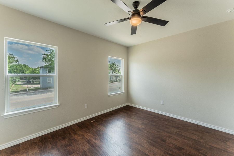 Spacious room featuring two large windows, a ceiling fan with integrated lighting, wood-finish flooring, and light-toned wall paint