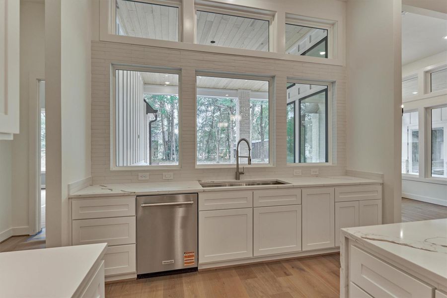 Dedicated prep and entertaining area featuring a separate sink, stainless dishwasher, and expansive windows showcasing serene outdoor views.