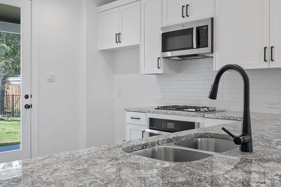 Kitchen with appliances with stainless steel finishes, white cabinets, light stone counters, and backsplash