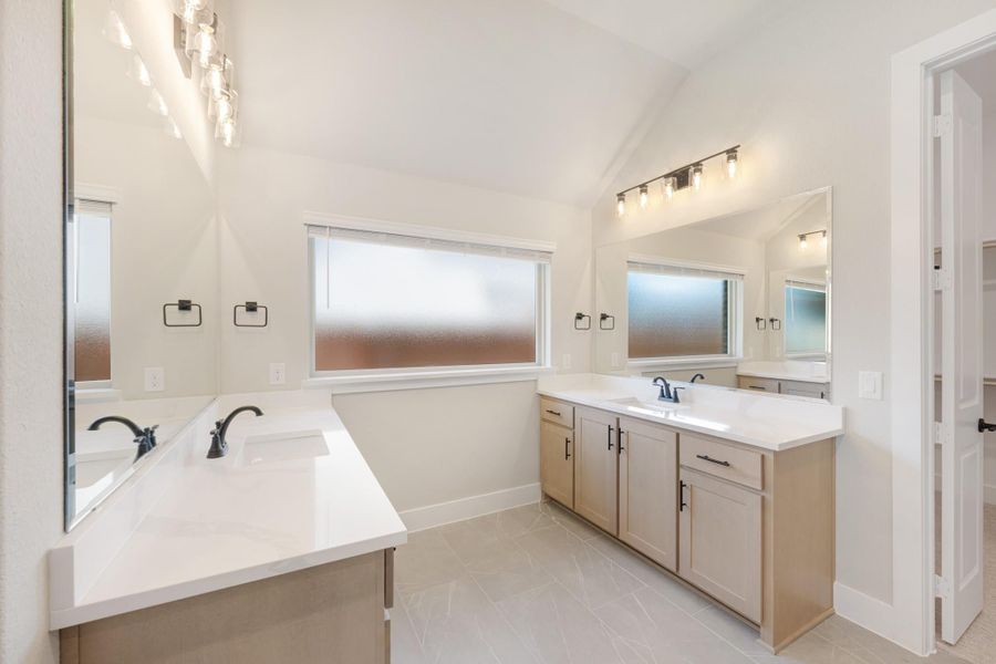 Master bathroom with dual vanities, white countertops, vaulted ceiling, and tile floors