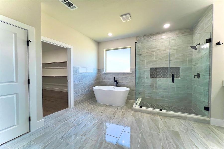 Bathroom with a walk in closet, a shower stall, a freestanding tub, and tile walls