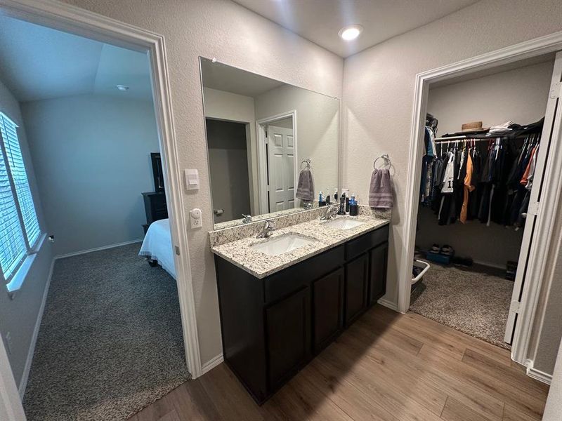 Bathroom featuring double vanity, a textured wall, light wood finished floors, a spacious closet, and ensuite bathroom