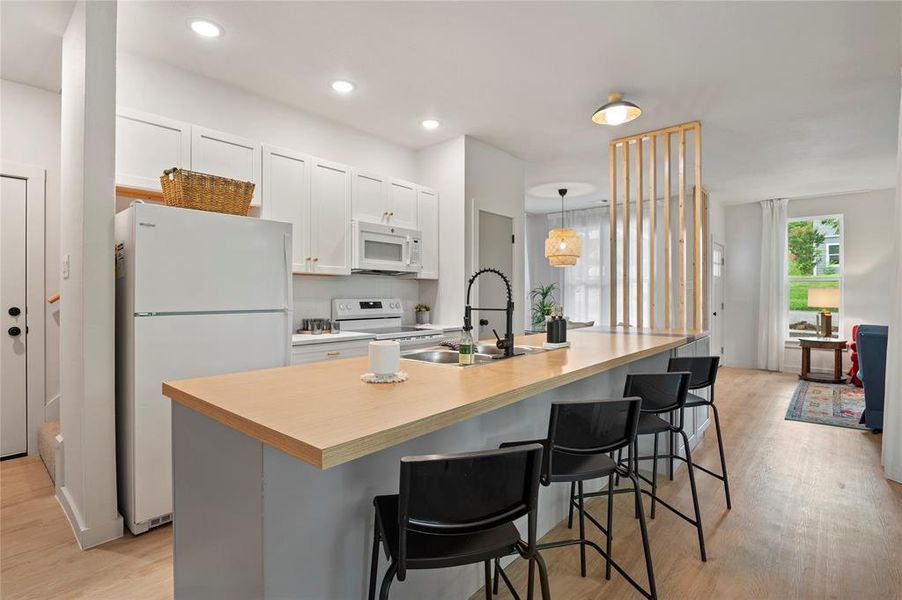 Kitchen with white cabinetry, an island with sink, white appliances, light hardwood / wood-style floors.