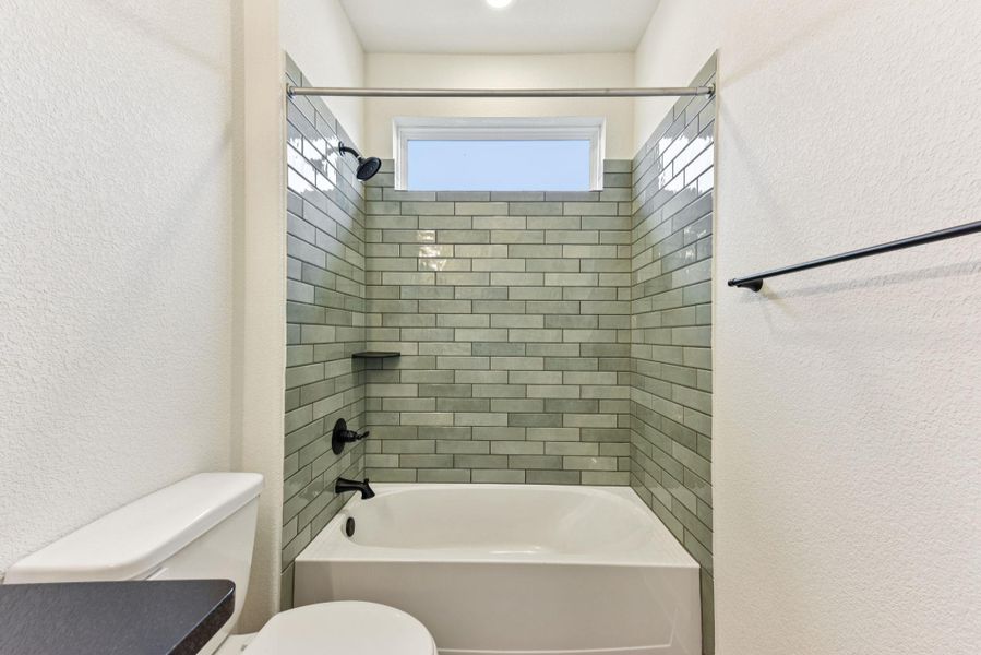 Bathroom with a textured wall and bathtub / shower combination