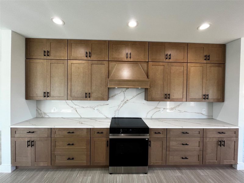 This kitchen features modern wooden cabinets with black handles, a sleek black stove, and elegant quartz countertops and backsplash. Recessed lighting enhances the clean, contemporary design.