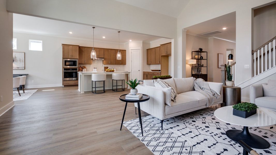 Large living room area with vaulted ceiling next to staircase and kitchen