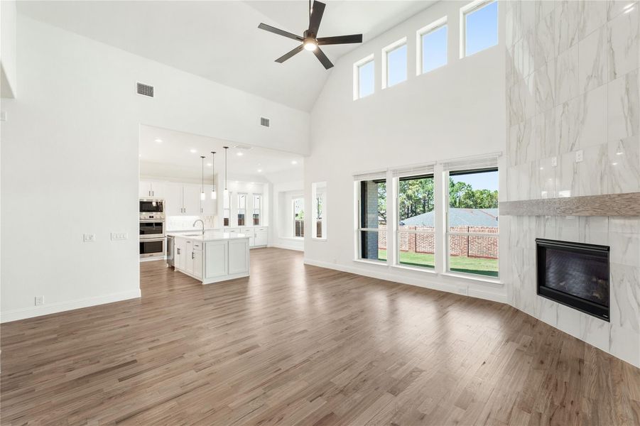 Open living area with vaulted ceiling, marble fireplace, hardwood floors, and open kitchen beyond