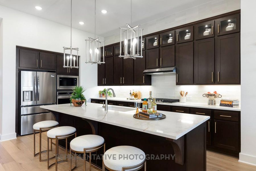 Kitchen with a breakfast bar area, light wood-style floors, dark brown cabinets, hanging light fixtures, and recessed lighting