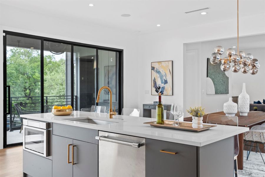 Modern kitchen featuring a large island with a sink and gold-toned faucet, light grey cabinetry, and stainless steel appliances