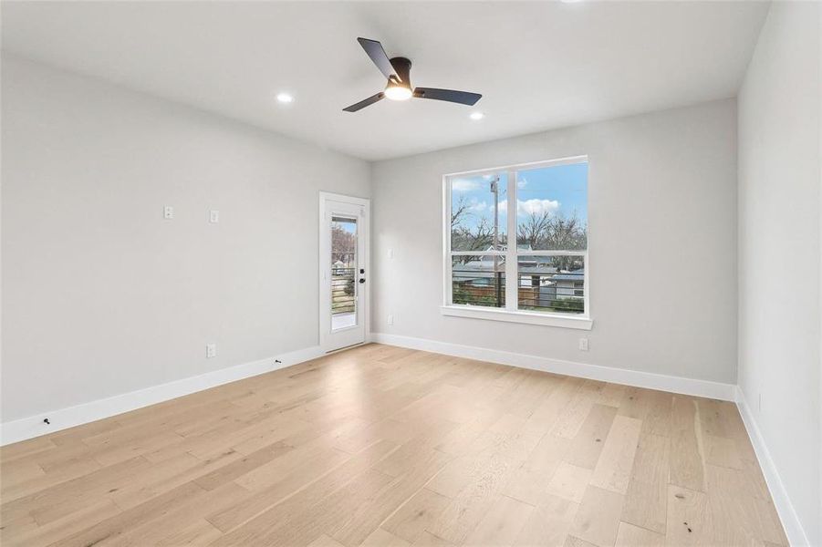 Spacious room featuring light wood-finish flooring, a contemporary ceiling fan with integrated lighting, recessed ceiling lights, a large window providing natural illumination, and a glass-paneled exterior door