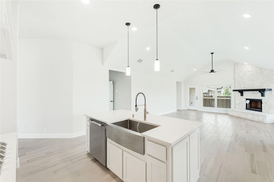 Kitchen island with farmhouse sink and pendant lights, open to living room with stone fireplace and vaulted ceiling