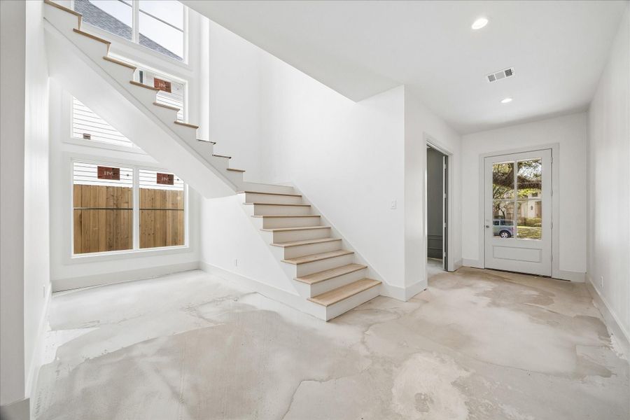 Light filled entry anchored by a striking staircase with clean modern lines and natural wood treads, complemented by expansive windows that bring in abundant natural light. The double height ceiling enhances the sense of openness, while the thoughtful layout offers seamless flow between the entry, study, and main living areas. Crisp painted walls, recessed lighting, and contemporary finishes create a bright and welcoming first impression, setting the tone for the rest of the home.