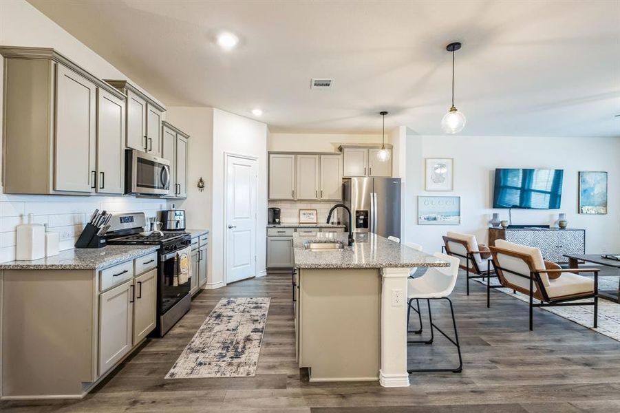 Kitchen with appliances with stainless steel finishes, light stone counters, hanging light fixtures, and sink