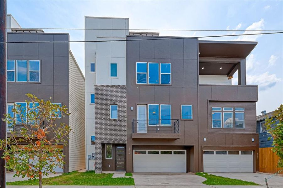 This modern, three-story townhouse features a sleek design with large windows, a brick accent facade, and an attached garage. It offers a spacious balcony on the top floor, perfect for outdoor living.