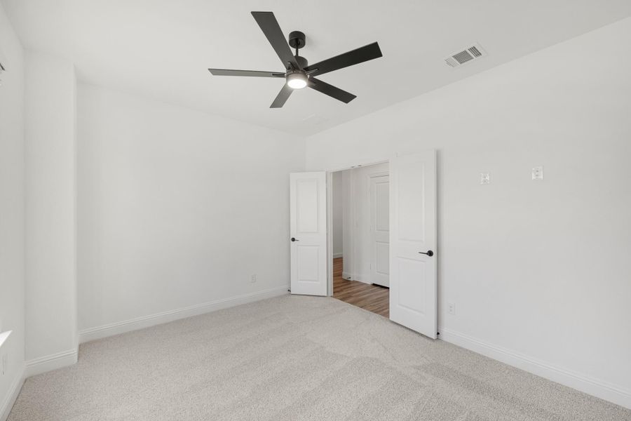 Empty bedroom with carpet flooring, black ceiling fan, and two white doors leading to adjoining rooms Empty bedroom with carpet flooring, black ceiling fan, and two white doors leading to adjoining rooms