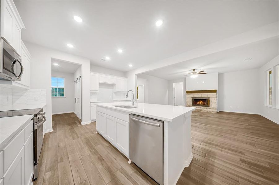 Kitchen with appliances with stainless steel finishes, ceiling fan, light wood-style flooring, white cabinets, and a stone fireplace Kitchen with appliances with stainless steel finishes, ceiling fan, light wood-style flooring, white cabinets, and a stone fireplace