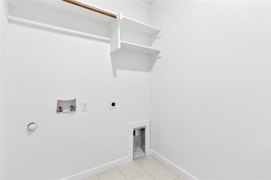 Dedicated laundry area featuring a built-in hanging rod, two upper storage shelves, washer and dryer hookups, and tiled flooring