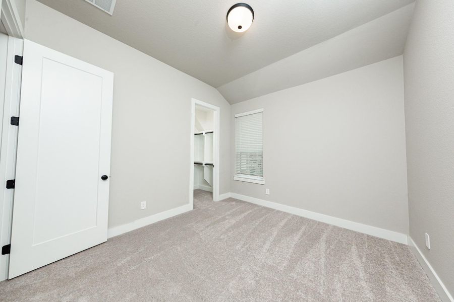 This secondary bedroom features a sloped ceiling, plush carpet flooring, a large window, a walk-in closet, and an ensuite secondary bathroom.