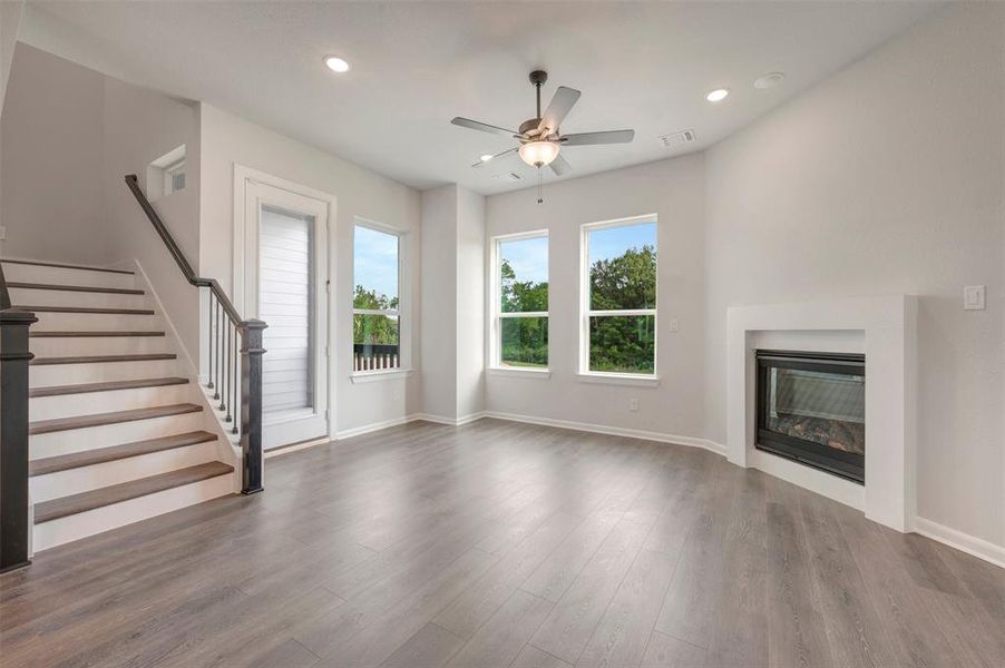 Living area featuring wood-finish flooring, a contemporary fireplace with a white surround, and three large windows Living area featuring wood-finish flooring, a contemporary fireplace with a white surround, and three large windows