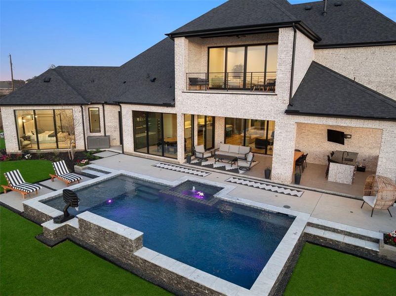Resort-style backyard retreat featuring a stunning pool, expansive patio, and covered outdoor living area designed for both relaxation and entertaining. The outdoor kitchen and lounge space seamlessly connect to the home, while the second-floor balcony above provides an additional private vantage point to enjoy the beautiful surroundings and lake views.