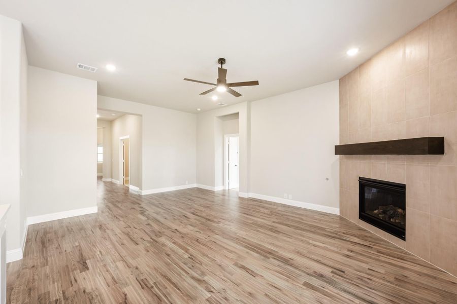 Open living room with hardwood floors, ceiling fan, and tile-surround fireplace with wood mantel Open living room with hardwood floors, ceiling fan, and tile-surround fireplace with wood mantel