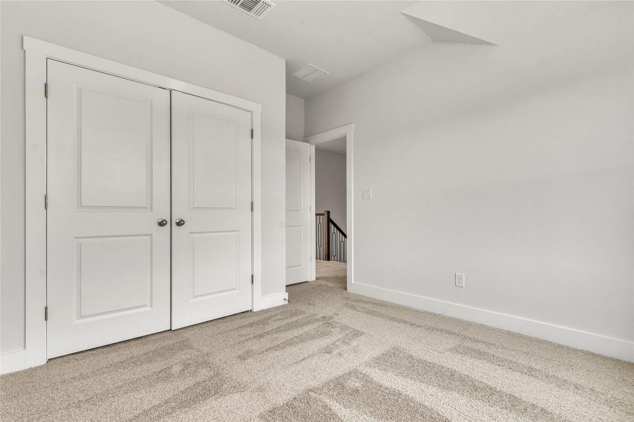 A quiet secondary bedroom features twin closets, soft carpet flooring, and access to a central staircase.