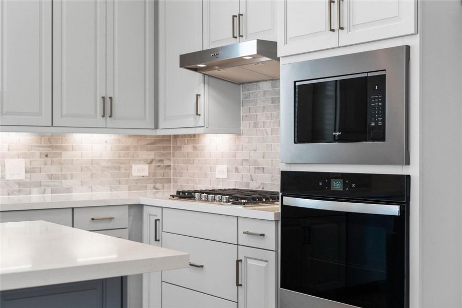The Whirlpool stainless steel appliances include a gas cooktop, vent hood, sensor cooking microwave, single wall oven with air fry capability and large capacity dishwasher. The stylish backsplash tile extends from the countertop to the upper cabinets, adding texture and visual interest.