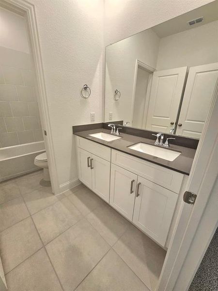 Full bathroom featuring double vanity, a textured wall, light tile patterned flooring, and tub / shower combination