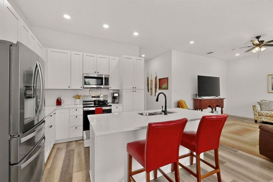 Contemporary kitchen featuring white shaker cabinetry, stainless steel appliances, a center island with sink, and wood-finish flooring