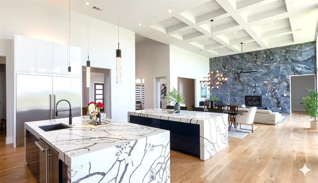 Open-concept interior featuring two waterfall-edge kitchen islands with veined countertops, integrated stainless steel appliances, and a prominent dark marble accent wall with a fireplace