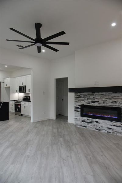 Unfurnished living room featuring a tile fireplace, light wood-type flooring, and ceiling fan