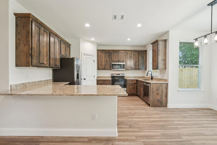 Kitchen with Vinyl Wood Plank floor, visible vents, a sink, a peninsula, and appliances with stainless steel finishes Kitchen with Vinyl Wood Plank floor, visible vents, a sink, a peninsula, and appliances with stainless steel finishes
