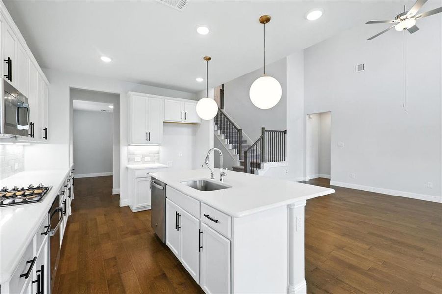 Stylish and sleek kitchen with modern lighting, wood floors, white cabinets and light countertops with gas cooktop and SS appliances.