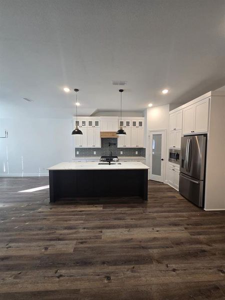 Kitchen featuring white cabinetry, pendant lighting, tasteful backsplash, stainless steel appliances, and a kitchen island with sink