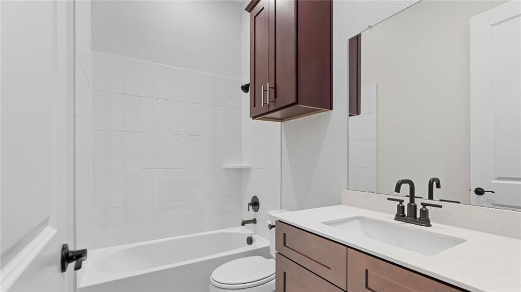 Modern bathroom featuring a white porcelain tub, white subway tile surround, dark bronze fixtures, and a vanity with a white countertop and dark wood-finish cabinetry