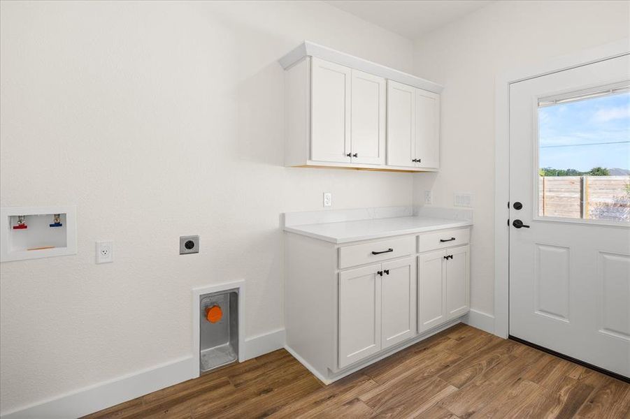 Dedicated laundry area featuring wood-finish flooring, white cabinetry with black hardware, a white countertop, and a white exterior door with an upper window
