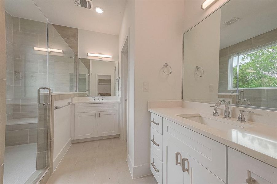 Double vanities with rectangular undermount sinks, quartz countertops, shaker style cabinets, modern pull handles, Glacier Bay polished nickel hardware and bath bar vanity lights adorn this primary bathroom.