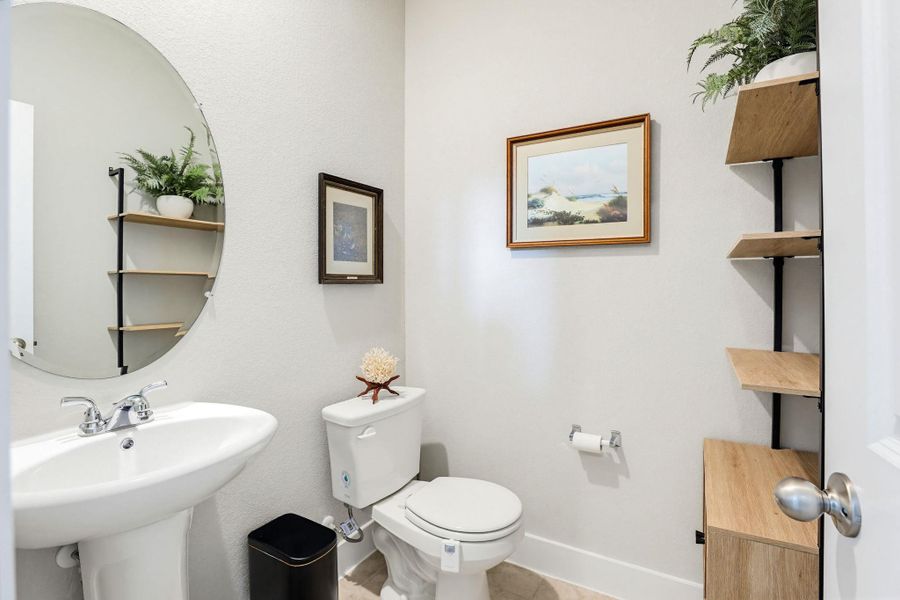 Bathroom featuring a pedestal sink, oval frameless mirror, and a toilet