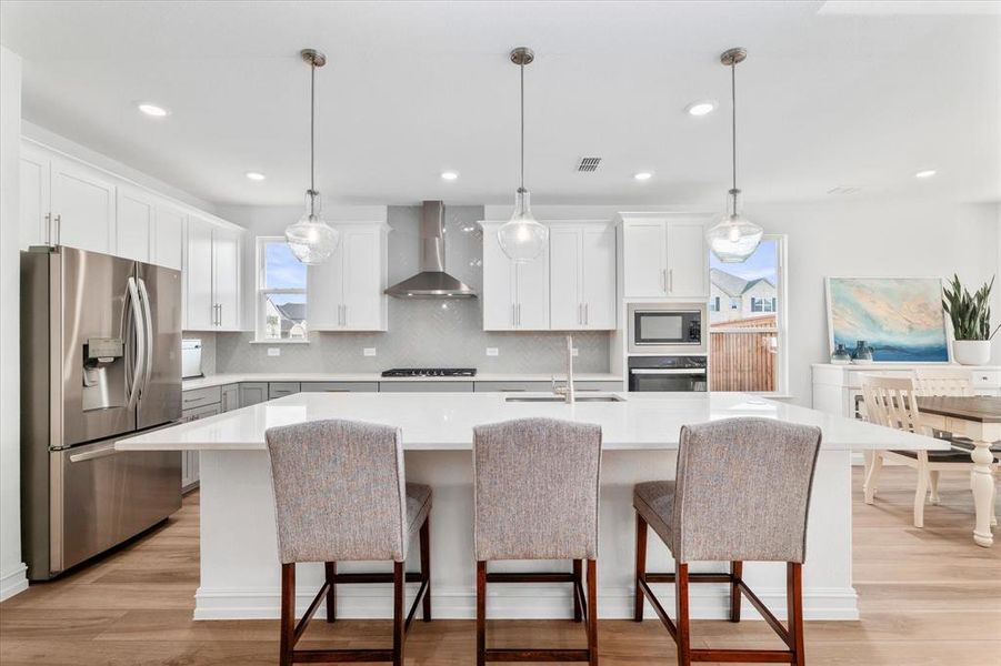 Open-concept kitchen featuring an oversized island with seating, stainless steel appliances, white cabinetry, recessed lighting, and wood-finish flooring