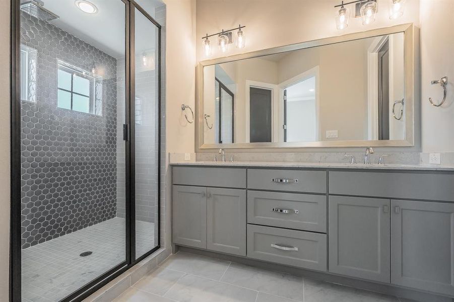 Contemporary bathroom featuring a spacious walk-in shower with dark hexagonal tile, a dual vanity with light gray cabinetry, and a large framed mirror with overhead lighting