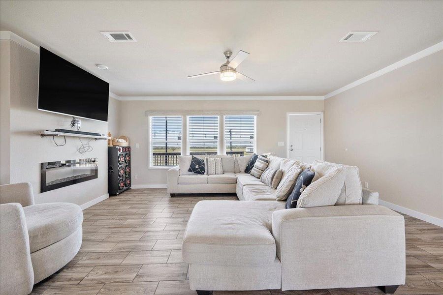 Living area featuring ornamental molding, ceiling fan, wood tiled floors, and a glass covered fireplace Living area featuring ornamental molding, ceiling fan, wood tiled floors, and a glass covered fireplace