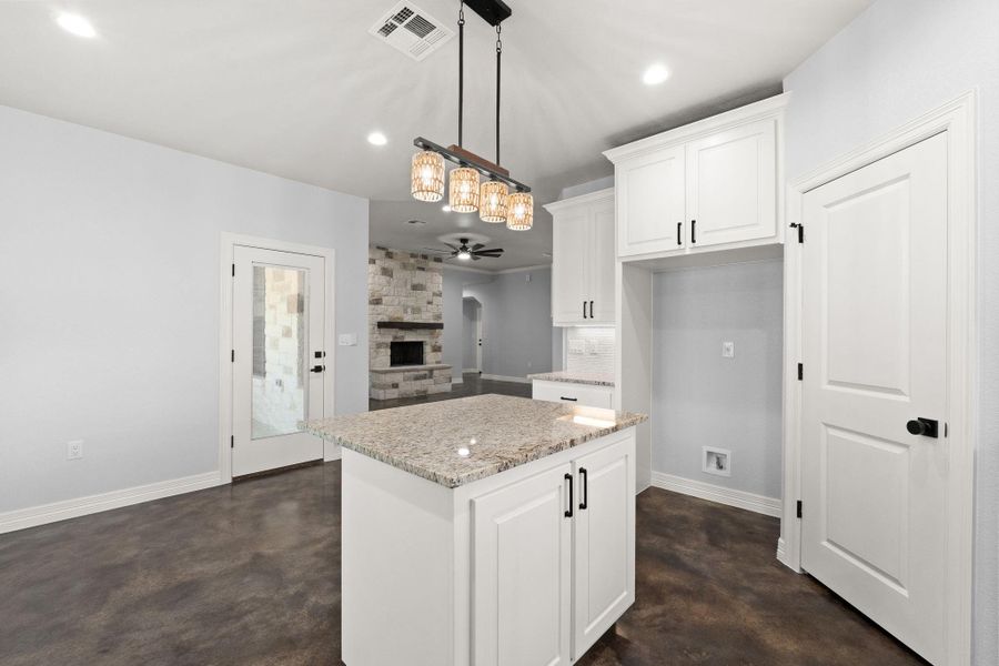 Kitchen with a stone fireplace, finished concrete flooring, recessed lighting, white cabinets, and light stone counters