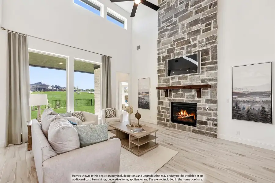 Living room with two-story stone fireplace, wood mantel, hardwood floors, and large windows with backyard view.