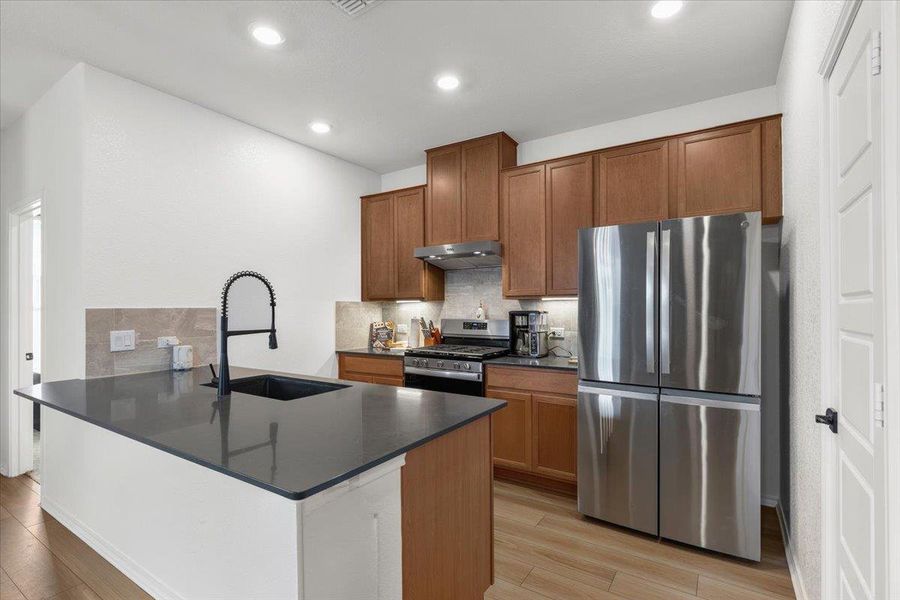 A contemporary kitchen showcasing rich wood-look cabinetry, stainless steel appliances, and a central island with a sleek sink.