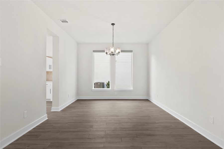 This photo showcases a bright dining room with light-colored walls, dark wood flooring, and a modern chandelier. It features a large window for natural light and an open doorway leading to the kitchen. This photo showcases a bright dining room with light-colored walls, dark wood flooring, and a modern chandelier. It features a large window for natural light and an open doorway leading to the kitchen.