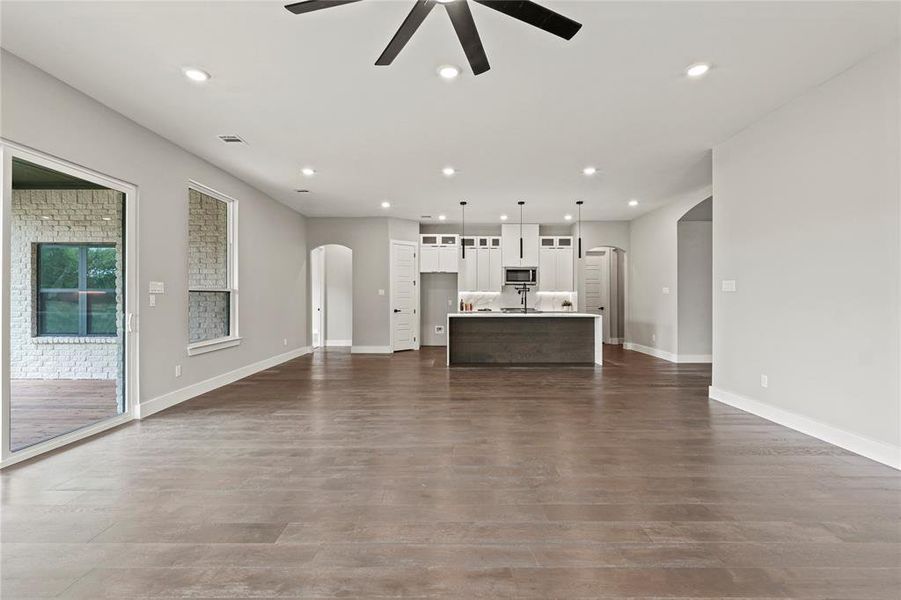 Living room with arched walkways, ceiling fan, dark wood-style floors, and recessed lighting