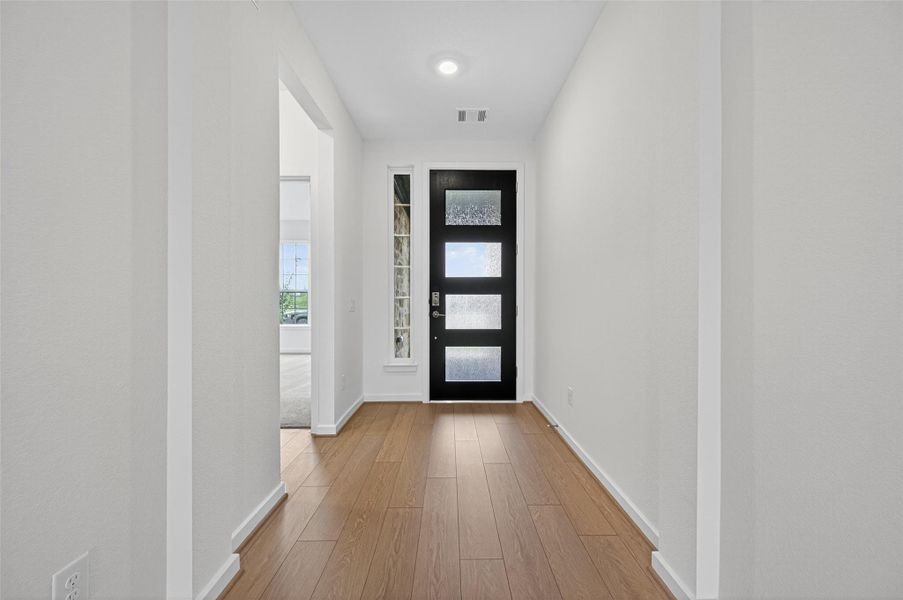 The sleek front door with frosted glass panels fills the entryway with soft natural light while adding a modern touch.
