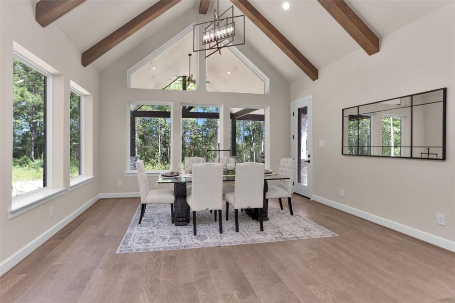 This inviting dining area features vaulted ceilings with wood beam accents, a modern chandelier and walls of picture windows that overlook the backyard and covered patio.